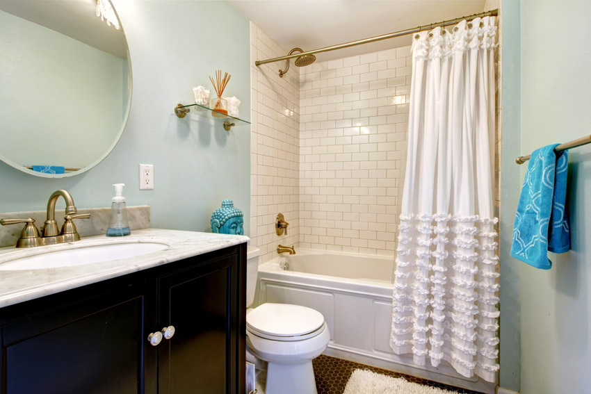 Bathroom with ruffle shower curtain, tile shower wall, toilet, mirror, and countertop