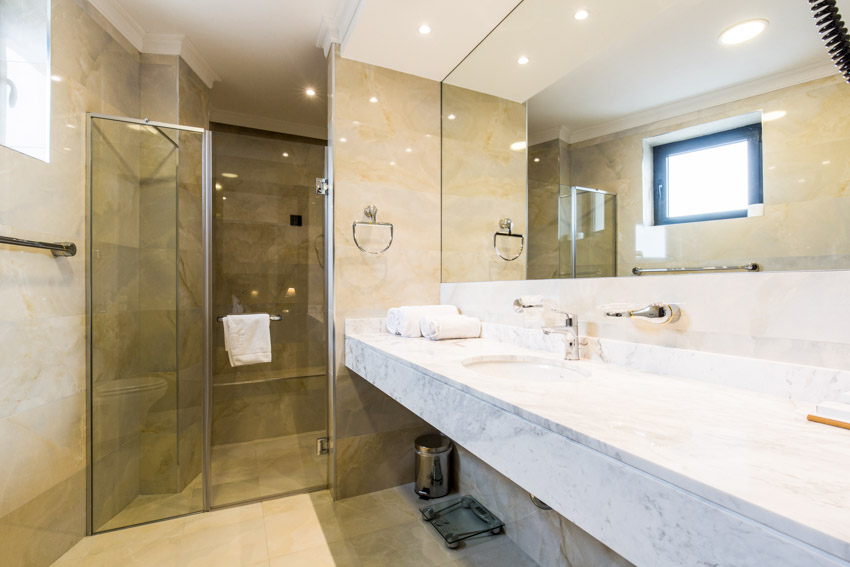 Bathroom with sandstone tile wall, quartz countertop, mirror, glass door, and shower area