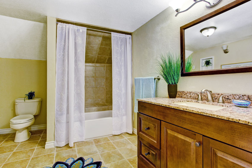 Bathroom with sheer curtain, tile floor, toilet, mirror, countertop, cabinets, and sink