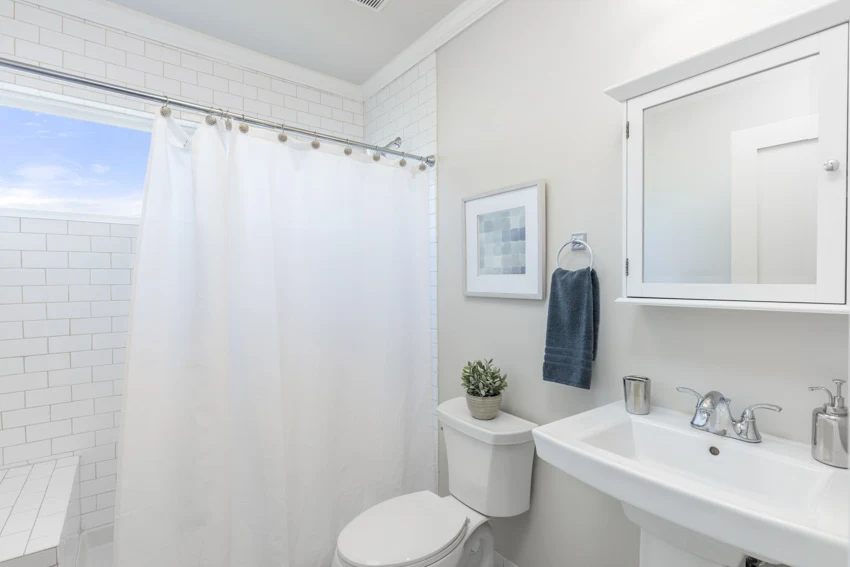 Bathroom with curtain, window, vanity, mirror, toilet, sink, and white wall 