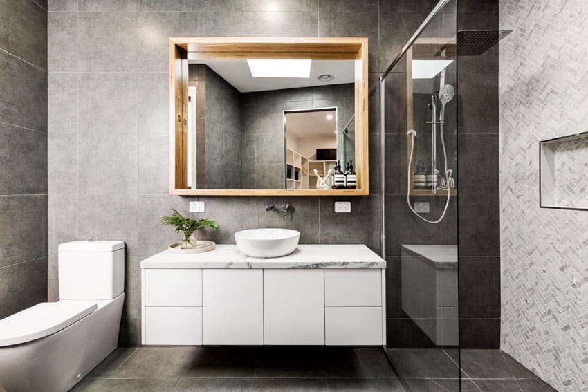 Bathroom with slate floor to ceiling tiles, floating vanity, toilet, mirror, glass divider, and shower