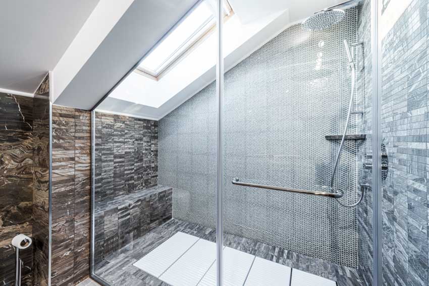 Bathroom with stone floor to ceiling tiles, glass door, shower area, and skylight window