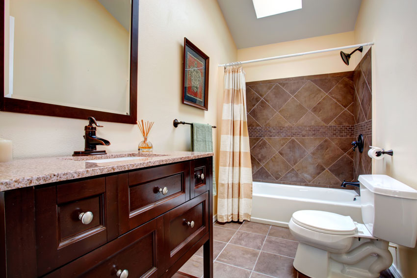 Bathroom with tile shower wall, shower curtain, drawers, countertop, mirror, toilet, and tile floors
