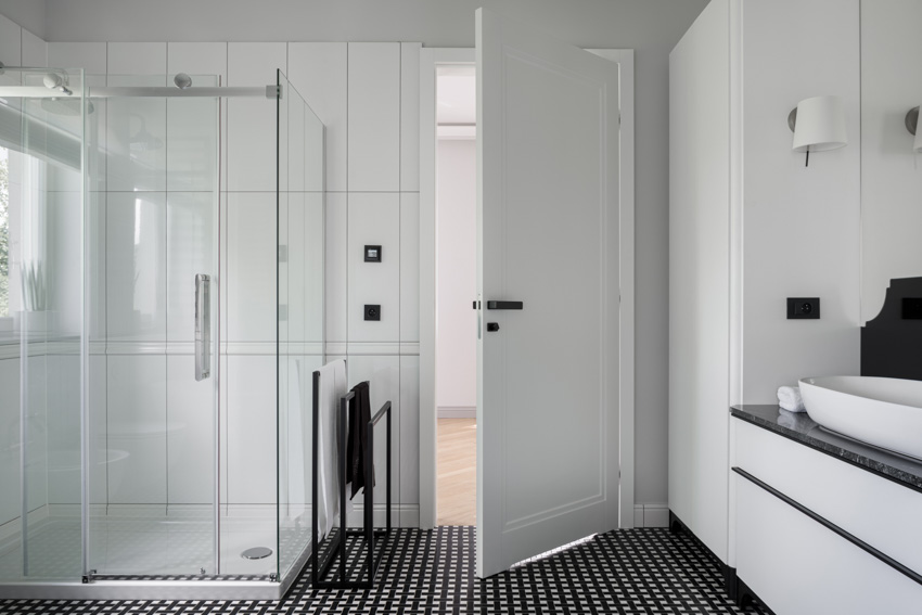 Bathroom with vertical large format tile shower, glass enclosure, black floor, door, sink, and white walls