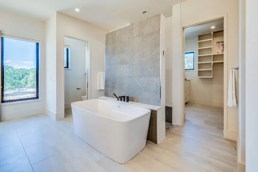 Bathroom with wallpaper accent wall and freestanding bathtub in center of bathroom next to walk through shower