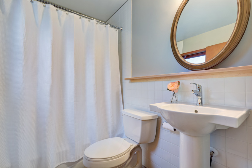 Bathroom with white shower curtain, round mirror, sink, and toilet