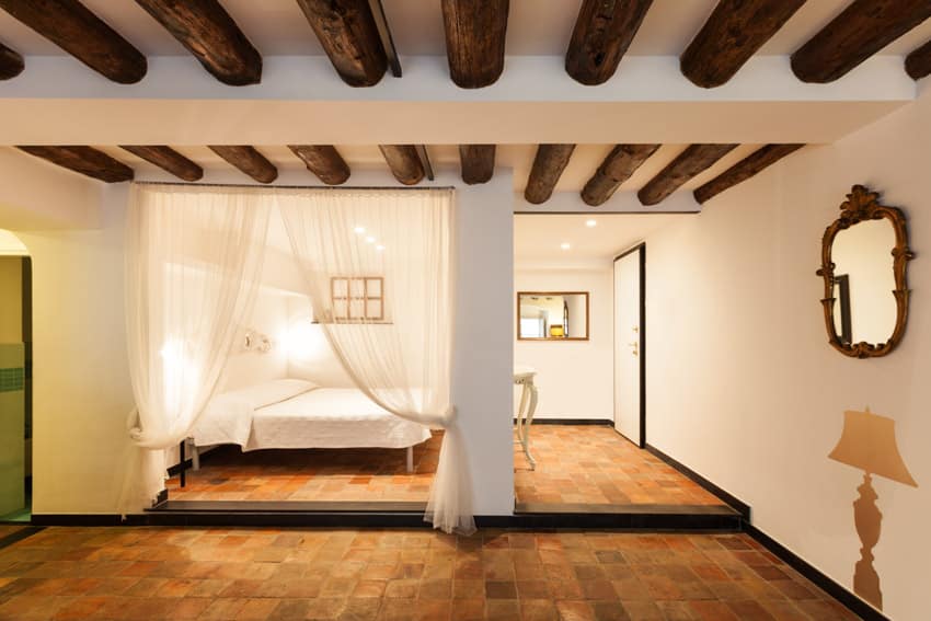 Bedroom with brick floor, exposed wood beam ceiling, bed, mirror, and pillar