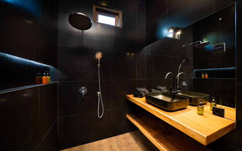 Black bathroom with floating wood, countertop, large format tile, shower wall, window, sink, faucet, and mirror