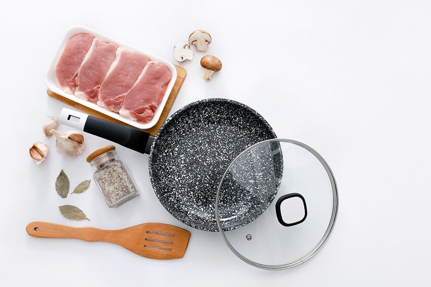 A black marble frying pan with raw meat and wooden spatula