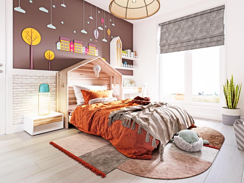 Children's bedroom with fabric Roman shades, window, indoor plant, bed, comforter, headboard, nightstand, and lamp