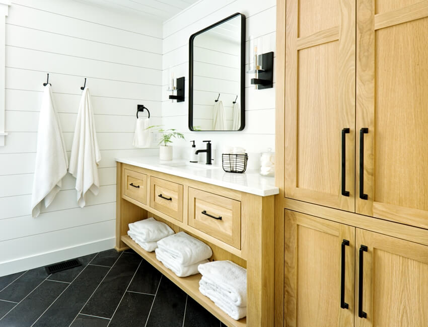 Clean bathroom with towels hanging in white shiplap walls, black tile floors and alder wood cabinets