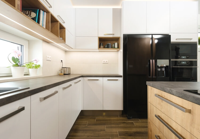 A contemporary kitchen with white euro style cabinets, black appliances and tiled floors