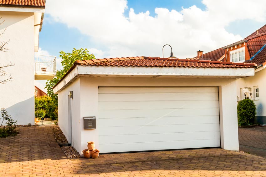 Detached drive through garage with orange shingle roof, and driveway