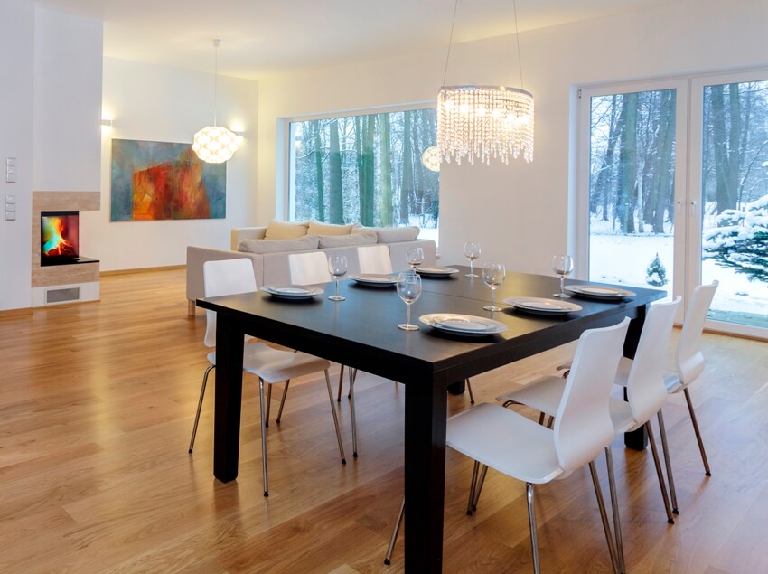 Dining room with laminate flooring, chandeliers, dining set and a view of trees with snow from the outside