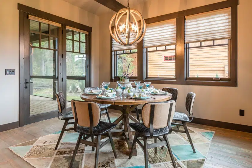 Dining room with roman shades, round table, chairs, rug, glass door, and hanging light