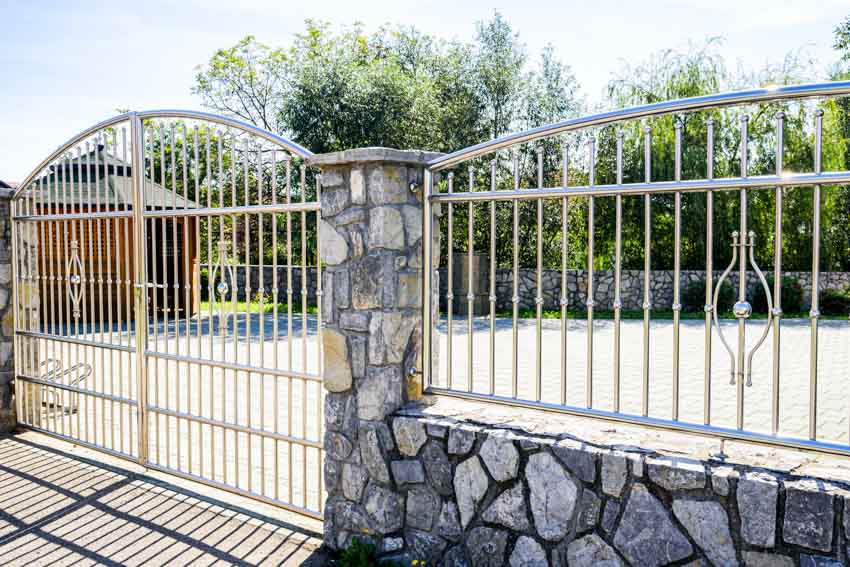 Driveway area of a house with an iron fence swing gate, and stone pillars