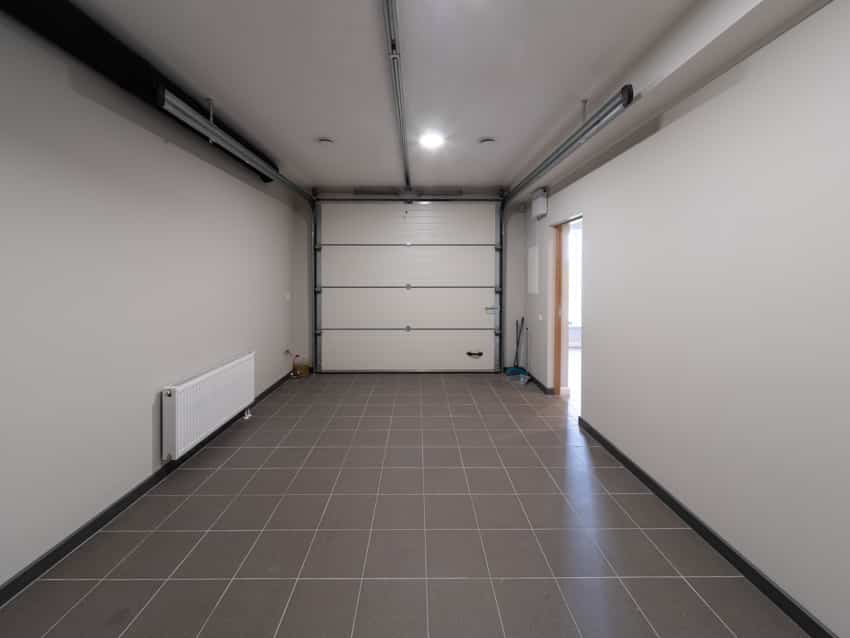 Empty garage with door, porcelain floor tiles, ceiling light, heater, and door opener