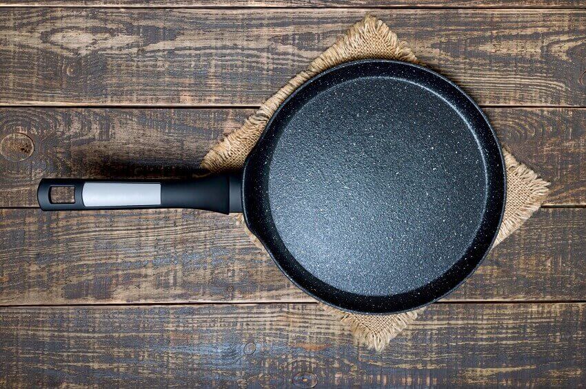 An empty granite frying pan with low sides and non stick coating on a wooden background 