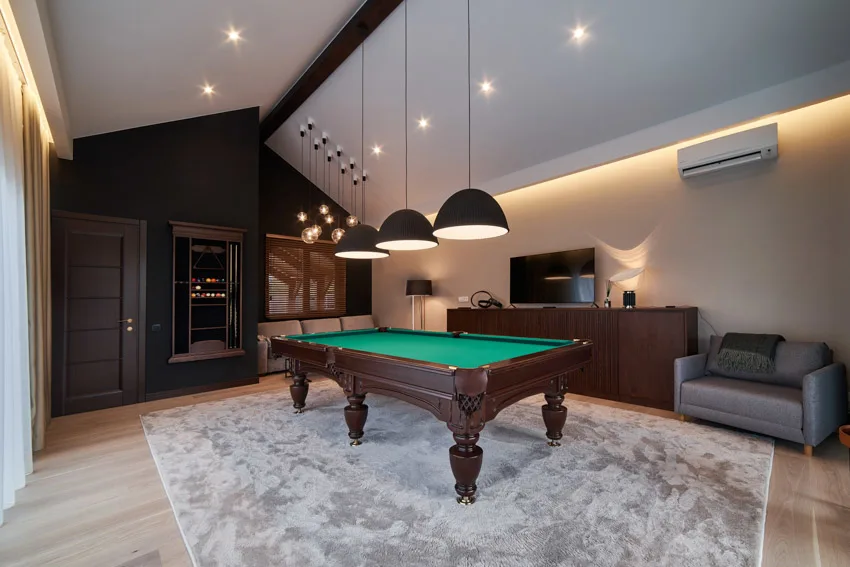 Game room with wood floor, rug pool, table, hanging lights, vaulted ceiling, dresser, and chair