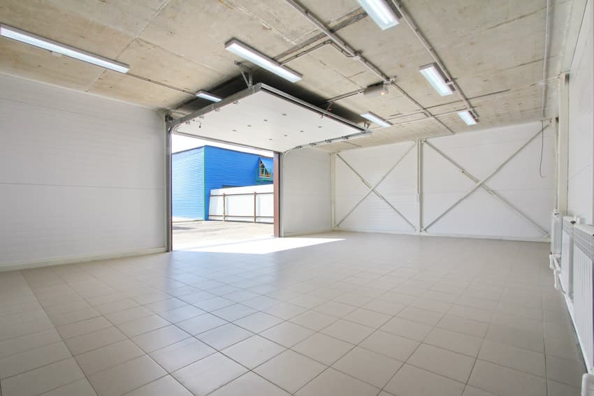 Garage with opened door, porcelain floor tiles, and overhead lights