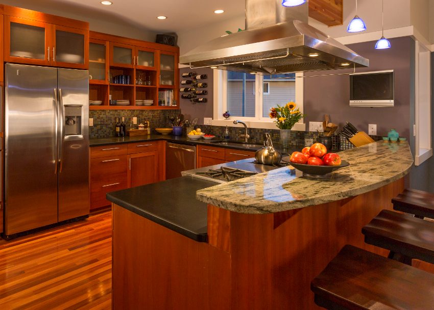 Home kitchen interior with wood cabinets and floors, bluestone countertops, accent lighting and stainless steel appliances