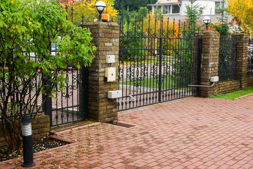 House entrance with large metal fence gate, and brick paver driveway