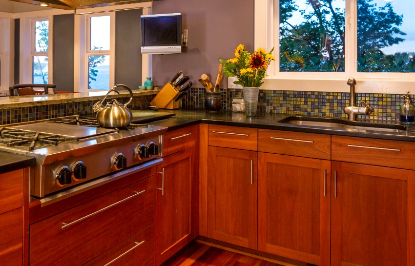 Kitchen interior with wood cabinets, gas stove, bluestone countertops, tile backsplash and view windows