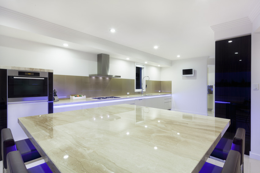 Kitchen with Taj Mahal quartzite slab table, range hood, backsplash, and ceiling lights