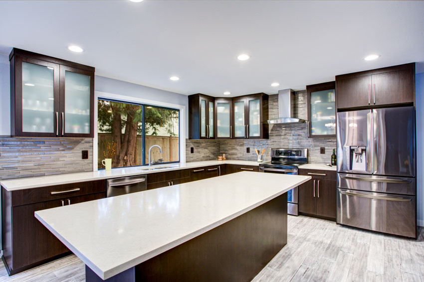 Kitchen with bamboo glass backsplash, countertop, center island, cabinets, windows, and range hood