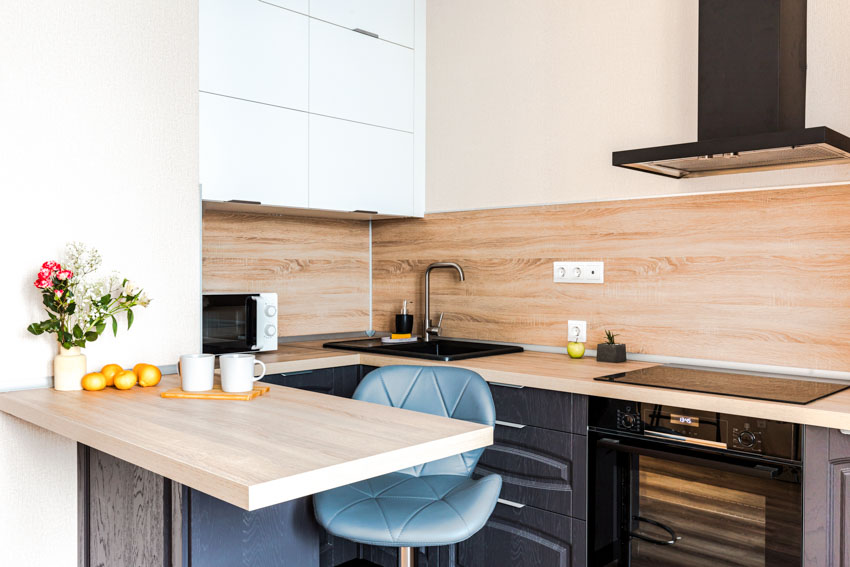 Kitchen with bamboo wood backsplash, induction stove, oven, range hood, sink faucet, and chair