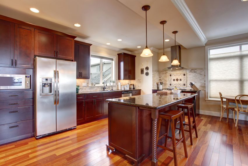 Kitchen with bar stools, bar dining area, countertops, refrigerator, hanging lights, countertops, and windows