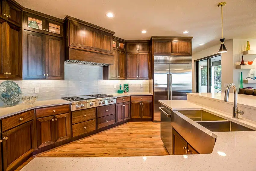 Kitchen with black Walnut cabinets, backsplash, countertops, sink, faucet, stove, range hood, and glass door