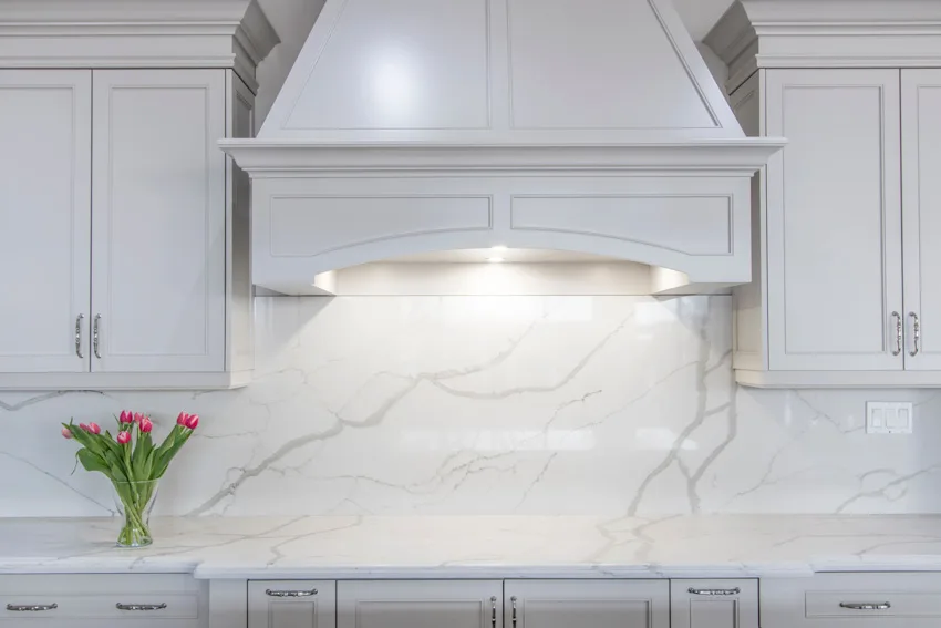 Kitchen with bookmatched quartz backsplash, white cabinets, countertop, and range hood