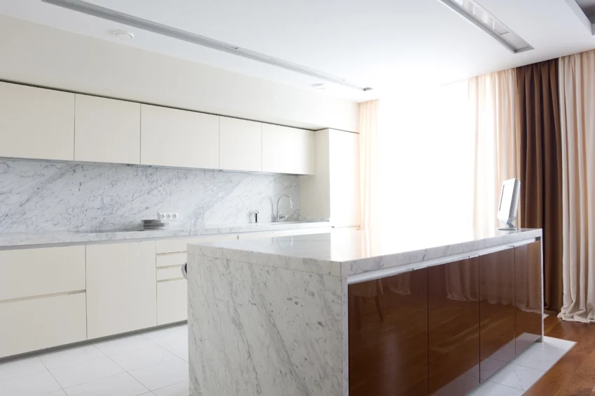 Kitchen with bookmatched Carrara quartz countertop, island, backsplash, white cabinets, and window curtains