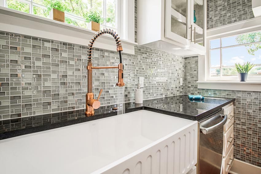 Kitchen with brass touchless faucet, mosaic tile backsplash, sink, countertop, cabinet, and windows
