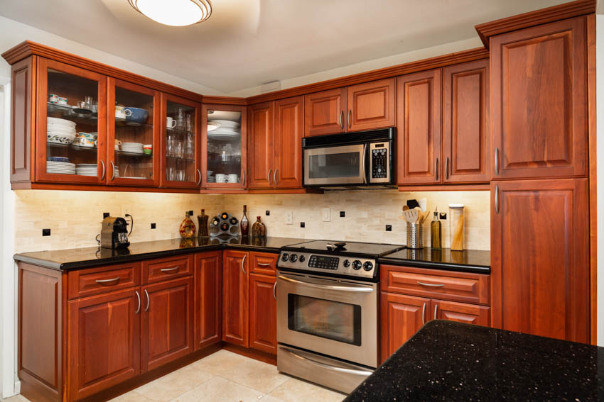 Kitchen with cherry wood cabinets, backsplash, countertops, oven, stove, and ceiling light