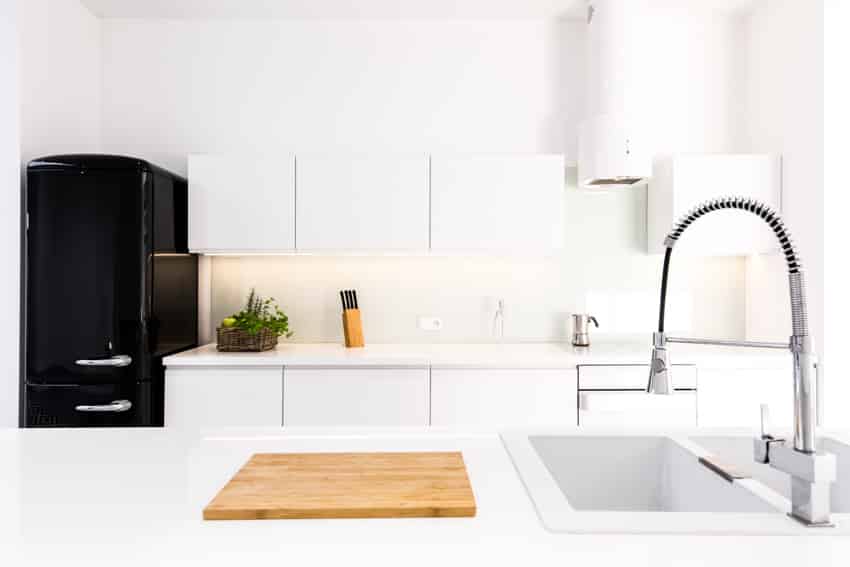 Kitchen with countertops, white cabinets, faucet, cutting board, and black refrigerator