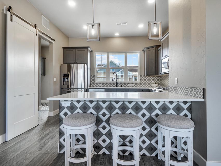 Kitchen with cushioned stools, countertop, peninsula seating, wood floor, barn door, window, and hanging lights