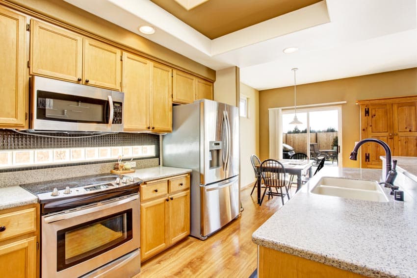 Kitchen with light colored Walnut cabinets, countertops, oven, backsplash, sink, faucet, table, chairs, and window