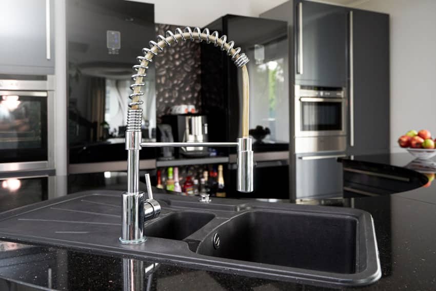 Kitchen with sink black countertop, backsplash, oven, and touchless faucet