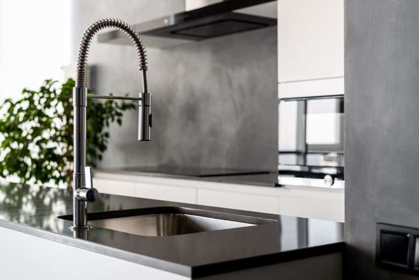 Kitchen with touchless faucet, countertop, concrete backsplash, and range hood