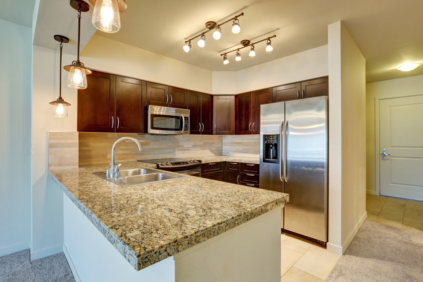 Kitchen with track lighting, granite countertop, mahogany cabinets, sink, faucet, pendant lights, and refrigerator