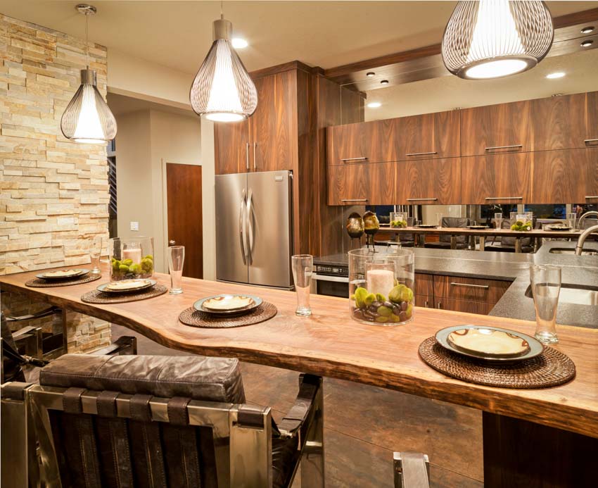 Kitchen with wood peninsula seating, plates, chairs, wood cabinets, accent wall, refrigerator, and pendant lights