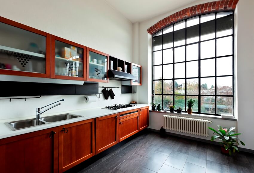 Kitchen with wooden cabinets, white tiled countertops with two sinks, dark porcelain and a big window