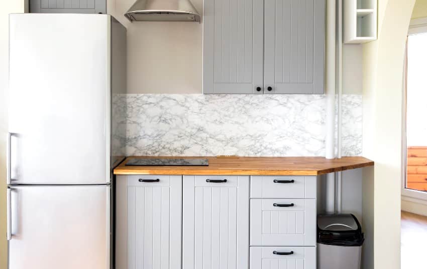 A light small kitchen with grey paint wooden grooved beadboard cabinets, stove and refrigerator