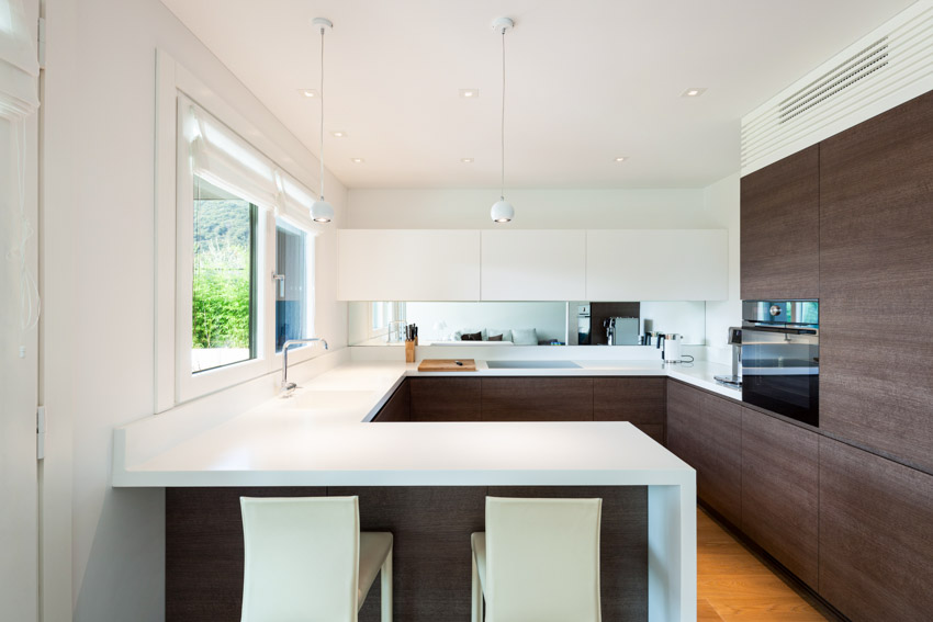 Minimalist kitchen with peninsula seating, wood cabinets, countertop, white walls, and window