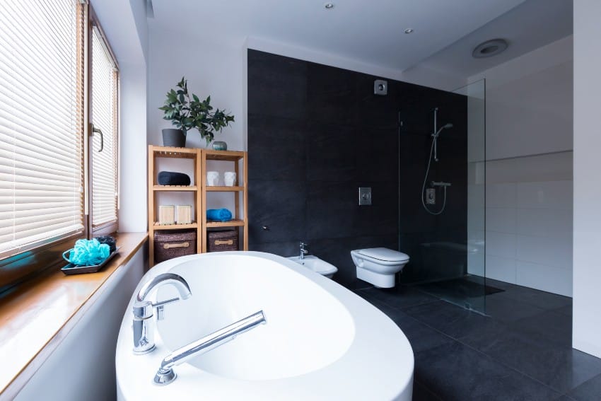 Modern and spacious bathroom with black accent wall, black tiles and transparent shower stall