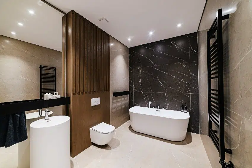 A modern bathroom design with large stone bath, black marble accent wall and tile floors