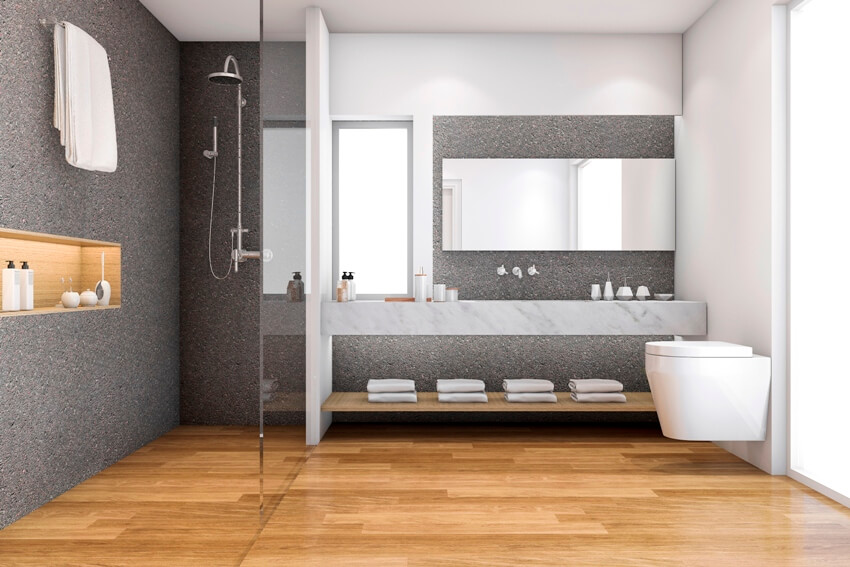 A modern bathroom with grey stone shower walls and backsplash, marble counter, mirror and wood looking vinyl planks flooring