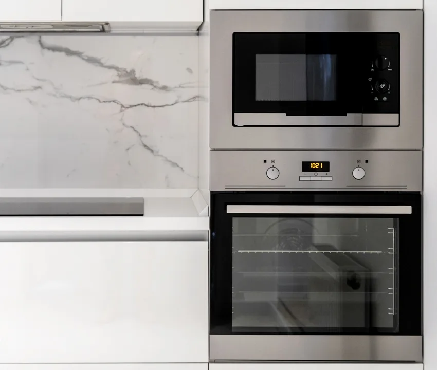 A modern kitchen with marble backsplash and built in steel microwave and oven